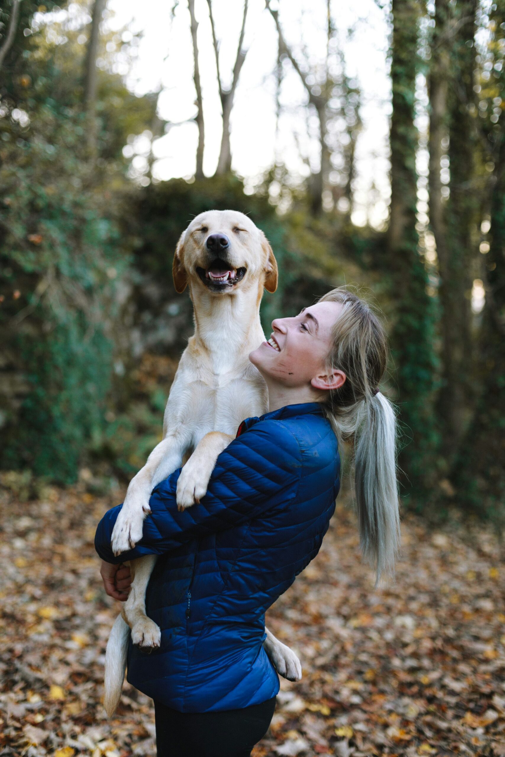 A dog owner laughing while holding her dog outdoors